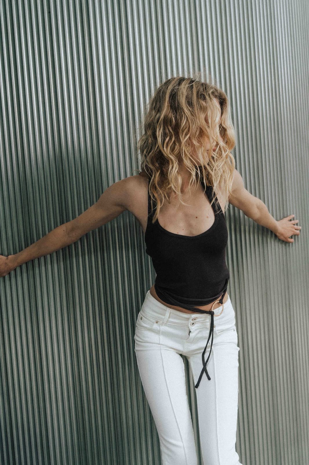 Blonde model against a corrugated metal wall, arms outstretched — NIKA, by Kenneth Kemp