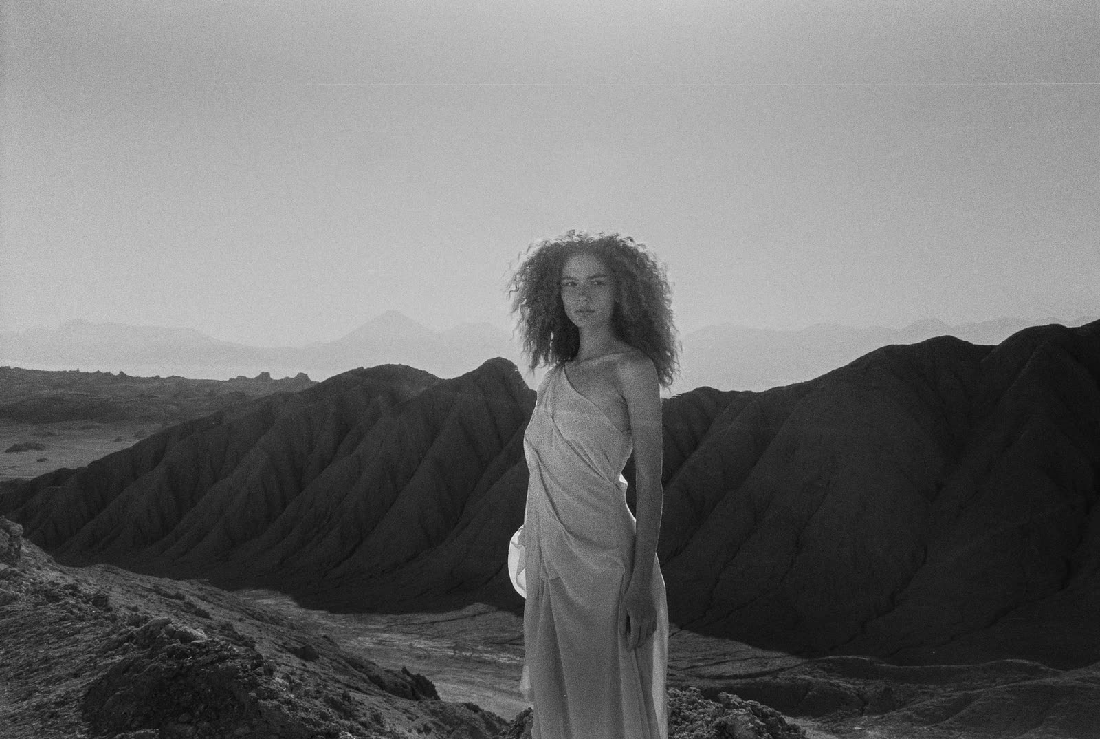 Black and white frame of a figure in a long dress in desert badlands — MASCAVO, by Kenneth Kemp