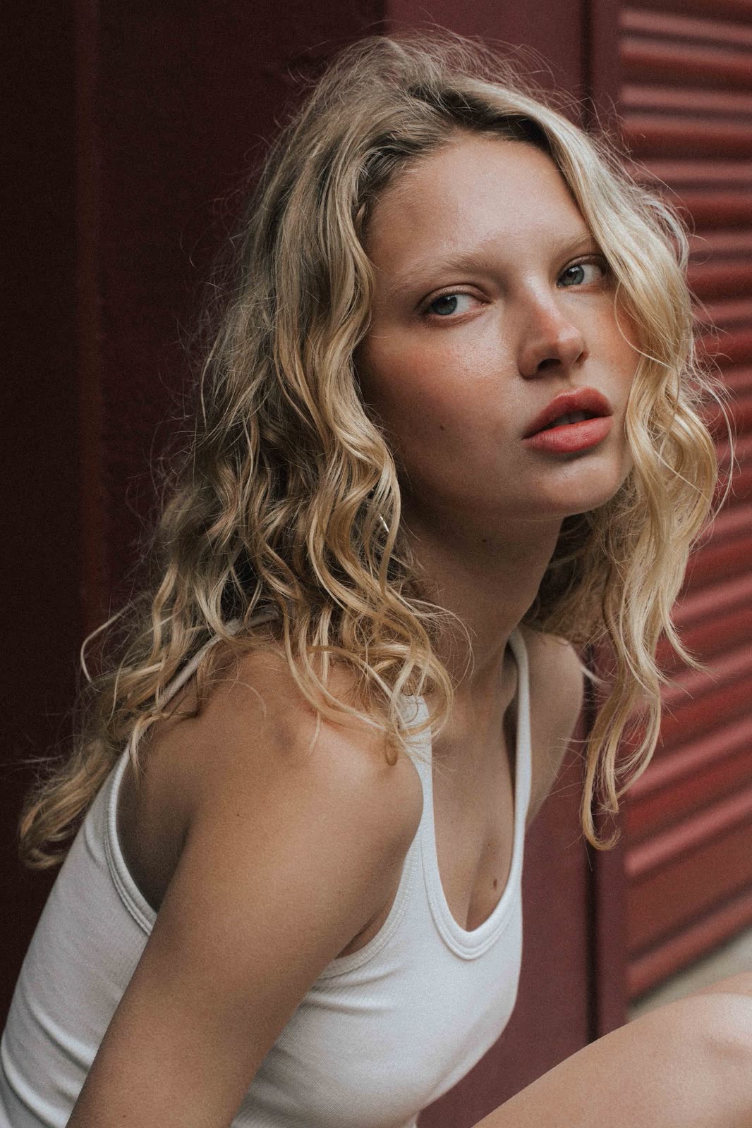 Blonde model in a white tank against red shutters — NIKA, by Kenneth Kemp