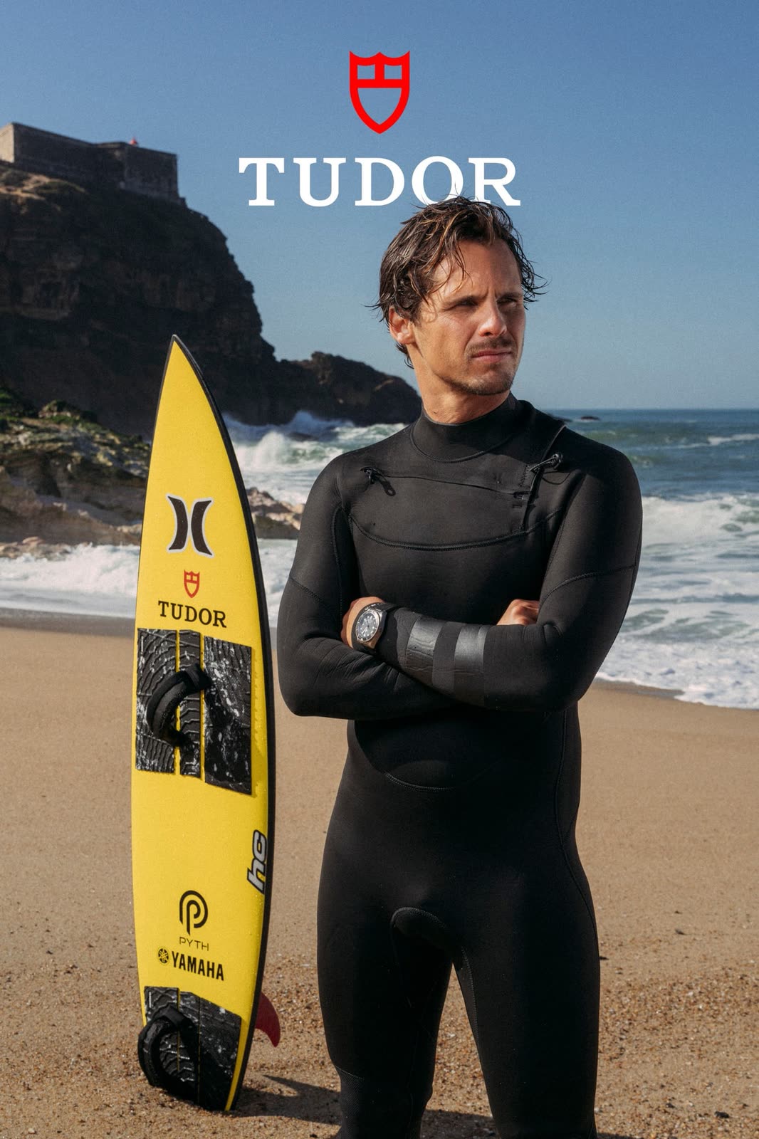 Surfer in a wetsuit beside a yellow board on the beach — TUDOR, by Kenneth Kemp