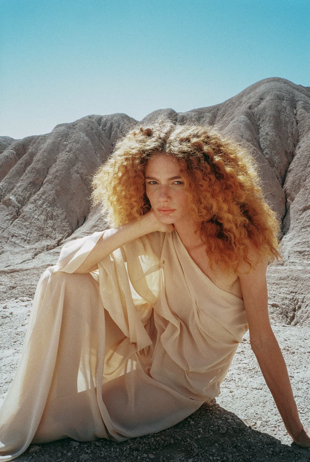 Model in a cream dress seated in desert badlands — MASCAVO, by Kenneth Kemp