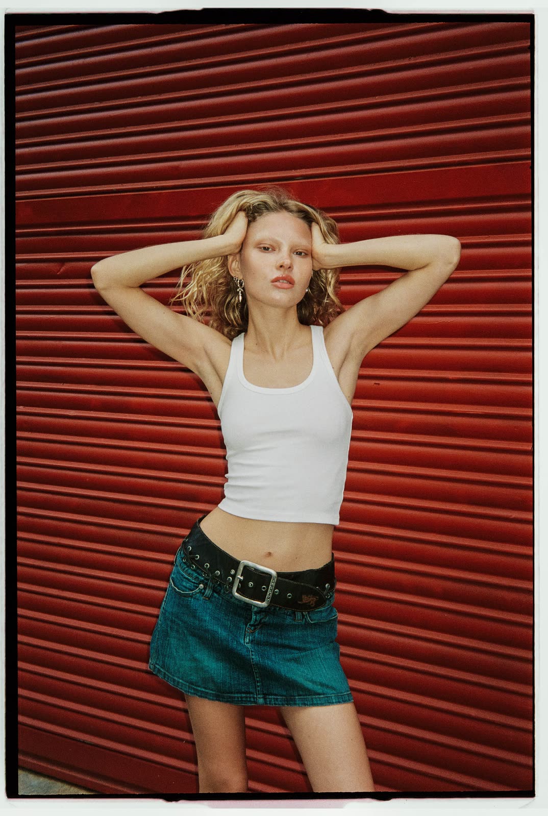 Blonde model in a white tank and denim skirt against a red shutter — NIKA, by Kenneth Kemp