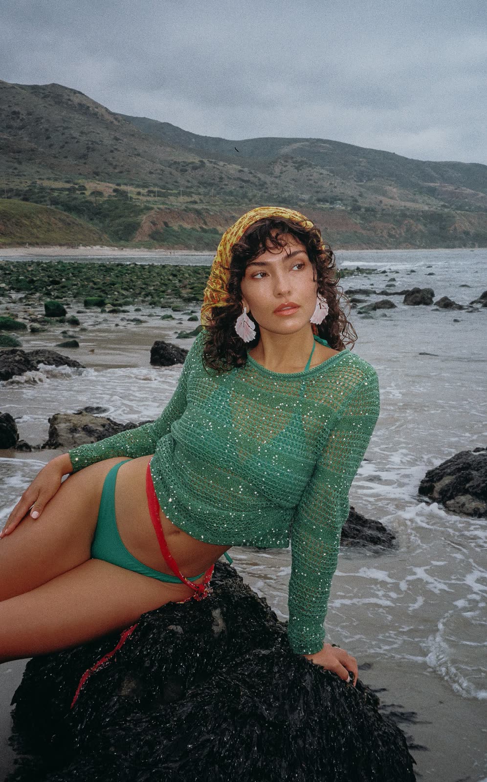 Model in a green knit top and headscarf seated on a rock at the waterline — SYDNEY, by Kenneth Kemp